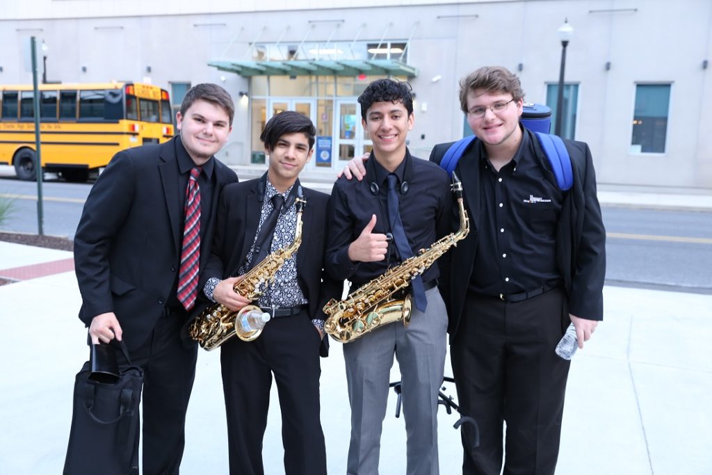 students pose for a picture outside of the school with their instruments